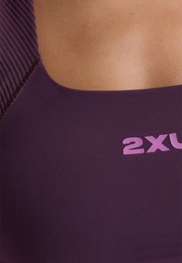 Ljubičasti sportski grudnjak s kvadratnim izrezom, rebrastim naramenicama i svijetloljubičastim logotipom. Glatka tekstura, dizajniran za udobnost.