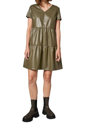 Robe en simili cuir vert olive avec des manches courtes, un col en V, un design à niveaux et un ourlet évasé. Assortie à des bottines noires à semelles épaisses.