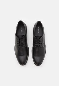 Chaussures en cuir noir avec une texture lisse, une forme pointue et un laçage. Présente des accents de couture subtils et une semelle intérieure rembourrée.
