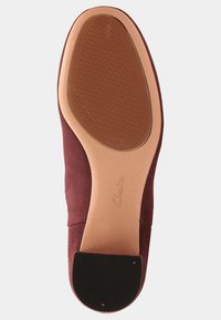 Podeszwa brązowego zamszowego buta na płaskiej podeszwie z teksturowanym gumowym bieżnikiem i czarną łatą na obcasie, z wytłoczonym logo Clarks w pobliżu łuku.