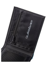 La cartera de tela negra cuenta con un bolsillo con cremallera, material texturizado y un acento azul. El logo de Quiksilver se muestra en gris en la superficie.