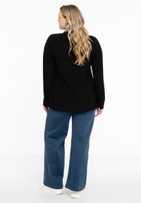 Zwarte blouse met lange mouwen en knoopmanchetten, gecombineerd met wijde blauwe jeans en witte sneakers, met een gladde stoftextuur.