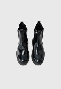 Bottines en cuir verni noir avec une finition lisse, dotées d'une semelle basse, de zips latéraux et de tirettes pour un enfilage facile.