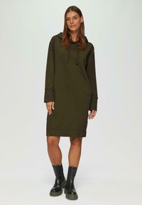 Olijfgroene hoodie-jurk van zacht materiaal, met lange mouwen, zijsplitten aan de zoom en gecombineerd met zwarte chunky enkellaarzen.