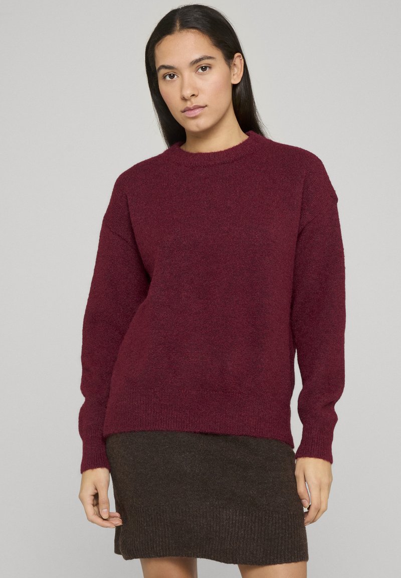 Pull en tricot bordeaux à manches longues, col rond et finition texturée, associé à une jupe côtelée en tricot marron foncé.