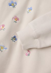 Lichtbeige sweatshirt met kleurrijke bloemenstickers in pink, blauw en wit. Rib gebreide manchet details benadrukken de textuur.