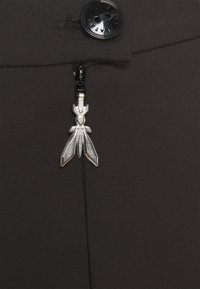 Gonna in tessuto nero con un bottone nero visibile e una cerniera dotata di un tirante decorativo argento a forma di insetto stilizzato.