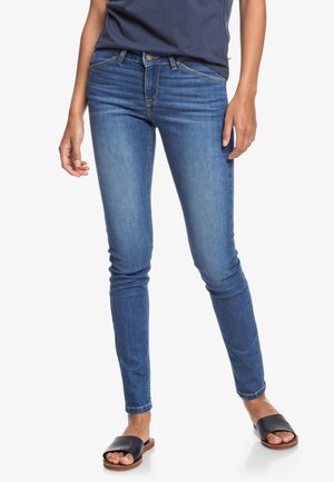 Dunne blauwe spijkerbroek van denim, met een middelhoge taille, vijf zakken en lichte vervaging. Draag ze met zwarte slippers.