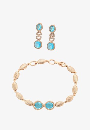 Złota bransoletka z teksturowanymi owalnymi ogniwami i niebieskim kamieniem w kształcie nieskończoności jako centralnym elementem, zestawiona ze złotymi kolczykami z zawieszkami z niebieskimi kamieniami o owalnym i poduszkowym szlifie.