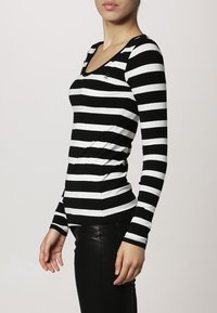 Schwarz-weißer gestreifter langärmeliger Oberteil mit V-Ausschnitt, ausgestattet mit einem taillierten Design und weichem Stoff. Auffälliges Markenlogo auf der Brust.