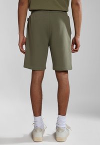 Khaki zelené šortky z měkké látky, s volným střihem, elastickým pasem a ohrnutým lemem, doplněné bílými teniskami a ponožkami.