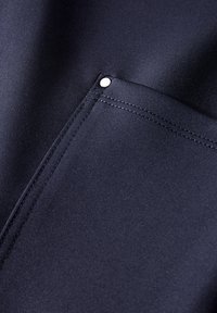 Tissu bleu marine avec une texture lisse, featuring une poche latérale sécurisée par un bouton-pression argenté. Couture visible le long du bord.