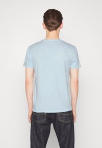 Svetle modré tričko s krátkým rukávem klasického střihu, měkká textura a volný střih, nošeno s tmavými džíny.