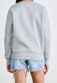 Grå fleece-tröja med ribbade muddar och nederkant, bärs med slitna denimshorts. Höjdpunkter inkluderar en rund halsringning och en avslappnad passform.