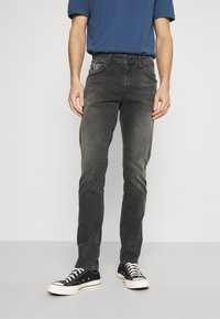 Jeans de mezclilla gris con corte slim, cinco bolsillos y un ligero desgaste. Combinados con zapatillas negras y una camiseta azul.