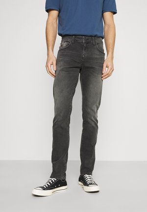 Jeans de mezclilla gris con corte slim, cinco bolsillos y un ligero desgaste. Combinados con zapatillas negras y una camiseta azul.