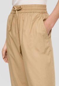 Beige elastische broek met een trekkoord in de taille, voorzien van zijzakken en een relaxte pasvorm, gemaakt van zachte, lichte stof.