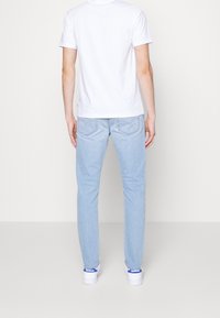 Light blue denim jeans with a straight fit, visible stitching, and back pockets, paired with a white T-shirt and white sneakers.