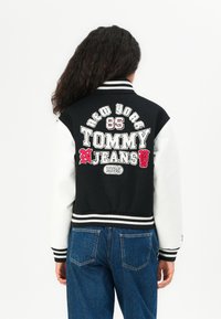 Giacca varsity bianca e nera con testo ricamato. Presenta polsini e orlo a costine, vestibilità oversize e un tessuto morbido e testurizzato.