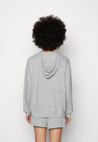 Felpa grigia realizzata in un tessuto morbido con un taglio rilassato, cappuccio con lacci e polsini a costine, abbinata a pantaloni corti coordinati.