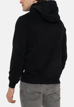 Hoodie noir avec une texture douce, doté d'une grande capuche, de poignets à bords côtes et d'une taille ajustée. Porté avec un jean gris slim.