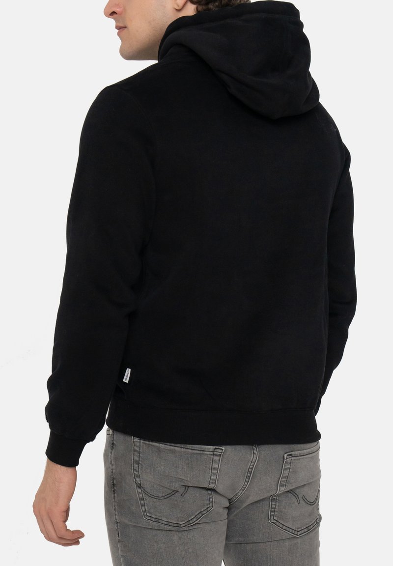Hoodie noir avec une texture douce, doté d'une grande capuche, de poignets à bords côtes et d'une taille ajustée. Porté avec un jean gris slim.