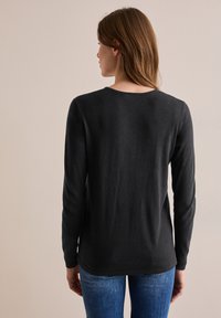 Maglietta nera a maniche lunghe con scollatura rotonda, realizzata in un tessuto morbido e liscio. Presenta una vestibilità tranquilla e una sottile trama.