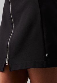 Svart kjol med siddragkedja och en liten logotagg, som framhäver dess trendiga design och tajta passform kring låren.