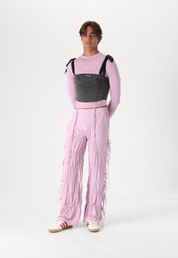 Čierny denímový cropped top s nastaviteľnými viazaniami, skombinovaný s svetloružovými, naťahovacími nohavicami. Biely tenisky s červenými pruhmi.