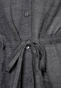 Grå stickad kofta med knäppning och dragsko i midjan. Har en texturerad tyg och rundad halsringning.