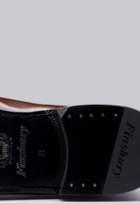 Bruine lederen schoenzool met een zwarte gestructureerde leren basis. Voorzien van ronde metalen studs en het geperste "Finsbury" merkteken. Klassiek ontwerp.