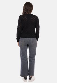 Maglione nero a maglia con un motivo ad pizzo aperto, scollatura rotonda e maniche lunghe, abbinato a jeans grigi a vita alta e sneaker bianche.