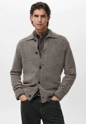 Cárdigan gris de lana con diseño de cuello, que presenta puños y dobladillo acanalados, cierre de botones y una textura suave. Llevado sobre una camisa oscura.