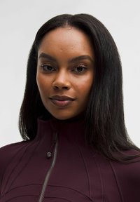 Burgundowa kurtka zapinana na zamek z wysokim kołnierzem, z przeszyciami oraz dyskretnym logo. Gładka, teksturowana tkanina.