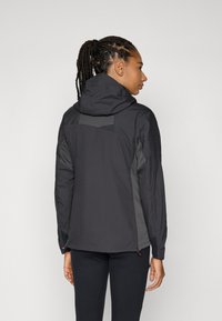 Schwarze Jacke mit Kapuze, ausgestattet mit grauen Akzenten, strukturierten Einsätzen und Reißverschlüssen am Saum. Glattes Material mit taillierter Passform.
