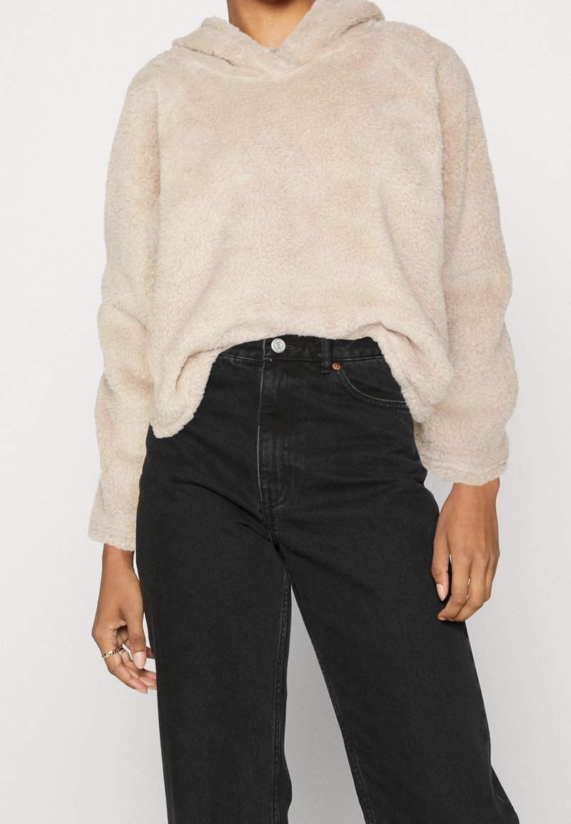 Pull à capuche beige duveteux porté avec un jean noir taille haute, recadré pour montrer le torse et les bras sans visage visible.