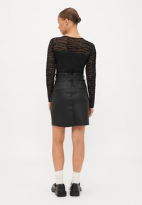 Μαύρη μπλούζα με μακριά μανίκια και υφή, διαφανής, σε συνδυασμό με μια μαύρη δερμάτινη μίνι φούστα με ζώνη στη μέση και δύο πίσω τσέπες.