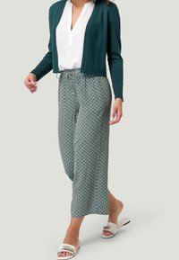 Cárdigan verde, blusa blanca, pantalones fluidos acampanados con un diseño de diamantes y sandalias blancas con una correa decorativa.