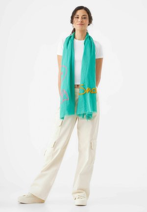 Écharpe turquoise en tissu léger, ornée d'une broderie rose et or avec un design de flamant rose et le texte "Smo", bords à franges.