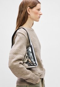 Black, shiny shoulder bag with a smooth, curved design. Worn over a beige knitted sweater with textured detailing on the sleeves.
