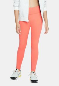 Leggings corallo brillanti con una texture liscia e una vita alta, abbinati a scarpe da ginnastica bianche e grigie con accenti colorati.