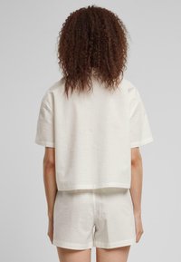 Hvit teksturert kortermet topp med løs passform, sammen med matchende shorts. Stoffet har et subtilt mønster som er synlig fra bakvinkelen.