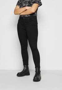 Jeans skinny negros con cintura de altura media, fabricados en un tejido suave, diseño de cinco bolsillos y piernas ajustadas, combinados con botas negras de tobillo.