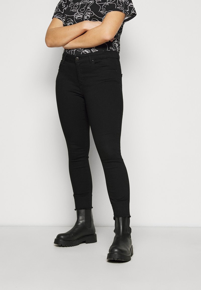 Jeans skinny negros con cintura de altura media, fabricados en un tejido suave, diseño de cinco bolsillos y piernas ajustadas, combinados con botas negras de tobillo.