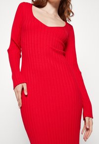 Abito rosso a maniche lunghe con scollatura rotonda, silhouette aderente e tessuto testurizzato, che offre una finitura liscia e una caduta morbida.