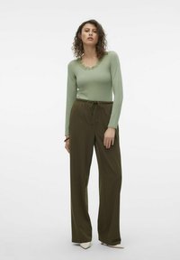 Haut vert clair à manches longues avec un décolleté festonné, associé à un pantalon évasé vert olive avec taille à cordon, présentant une texture minimale.