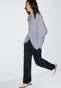 Koszula na guziki w niebiesko-białe paski, zestawiona z czarnymi spodniami. Strój ma luźny krój i lekką fakturę.