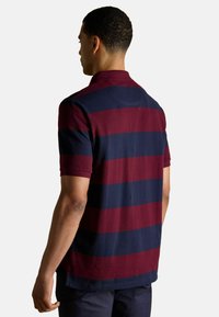 Bordo un jūras zils svītrains polo krekls ar īsām piedurknēm, apkakli un taisnu apakšmalu. Gluda tekstūra un ikdienišķs dizains.