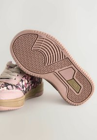 Scarpa sportiva rosa con tomaia in tessuto floreale, suola ammortizzata e suola in gomma decorata con scanalature circolari e un accento dorato.