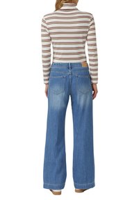 Bluzka w paski z długim rękawem w kolorze białym i brązowym; szerokie niebieskie dżinsy z wykończeniem w stylu sprania; dwie kieszenie z tyłu oraz skórzana naszywka na pasku.